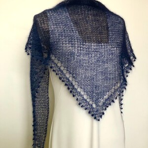 May include: A dark navy blue triangular shawl featuring a loose, open-knit texture with a fuzzy appearance. The edges of the shawl are finished with a decorative border of small, dangling loops, creating a delicate and airy look for this accessory.