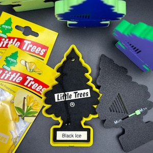 Op de afbeelding: Een assortiment Little Trees luchtverfrissers in verschillende kleuren. De afbeelding toont verschillende boomvormige luchtverfrissers, waaronder een zwarte met de tekst "Black Ice" en gele verpakking. De verpakking toont het Little Trees logo en productinformatie.