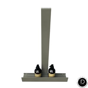 May include: A matte gray metal wall-mounted shelf featuring a tall vertical back panel and a horizontal base tray. Two dark brown plastic pump bottles with beige labels are positioned side-by-side on the shelf tray. The design is simple and functional.