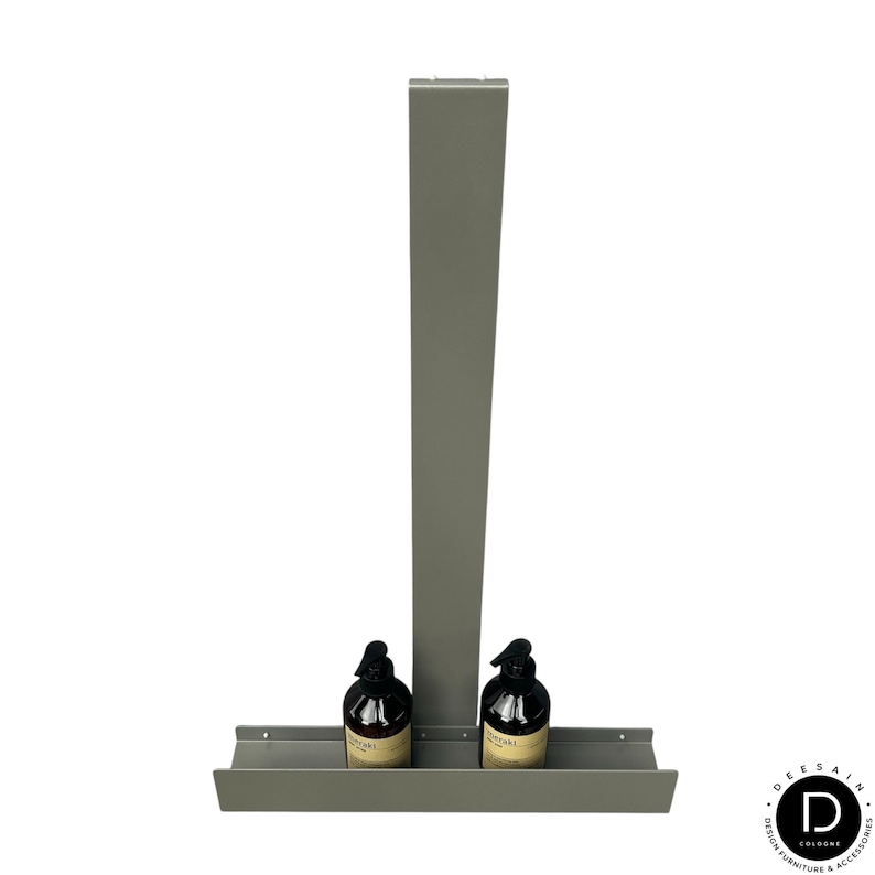 May include: A matte gray metal wall-mounted shelf featuring a tall vertical back panel and a horizontal base tray. Two dark brown plastic pump bottles with beige labels are positioned side-by-side on the shelf tray. The design is simple and functional.