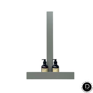 May include: A matte sage green metal wall-mounted shelf featuring a vertical support bar and a horizontal base. Two dark amber glass pump bottles with black dispensers and beige labels are positioned on the shelf base, one on each side of the bar.