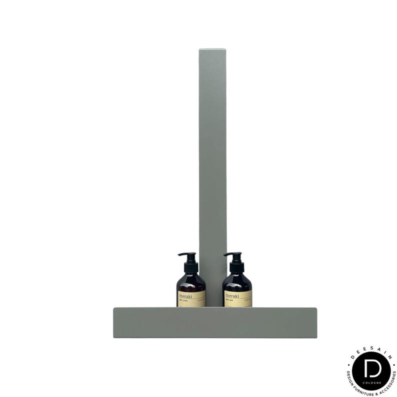 May include: A matte sage green metal wall-mounted shelf featuring a vertical support bar and a horizontal base. Two dark amber glass pump bottles with black dispensers and beige labels are positioned on the shelf base, one on each side of the bar.