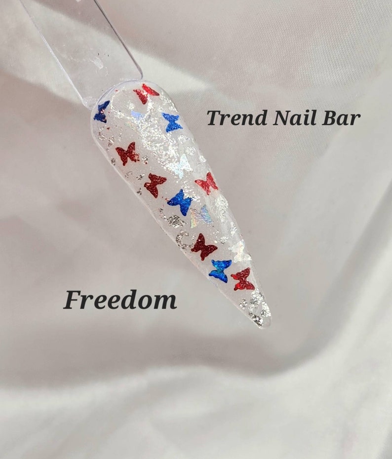 May include: A white nail with red, white, and blue butterfly nail art. The nail art is on a white background with the text "Trend Nail Bar" and "Freedom".