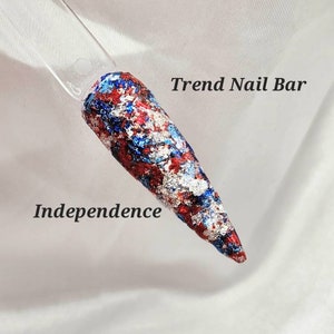 May include: A red, white, and blue nail polish with a metallic finish. The polish is called "Independence" and is from Trend Nail Bar.