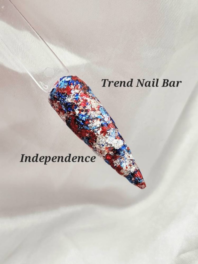 May include: A red, white, and blue nail polish with a metallic finish. The polish is called "Independence" and is from Trend Nail Bar.