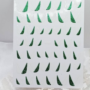 May include: A sheet of white sticker paper with multiple green glitter Christmas tree stickers. The stickers are in the shape of a triangle with a rounded top.