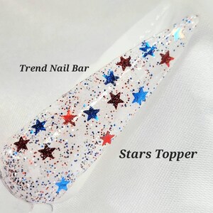 May include: A clear nail polish topper with red and blue glitter stars. The text "Trend Nail Bar" and "Stars Topper" are visible in the image.