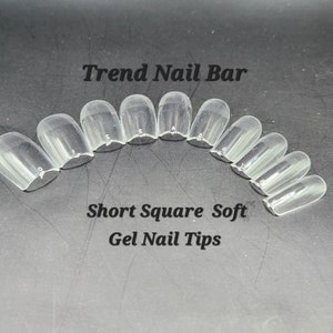 May include: Clear, short square soft gel nail tips arranged in an arc. The text "Trend Nail Bar" is at the top, and "Short Square Soft Gel Nail Tips" is at the bottom. Each tip is numbered.
