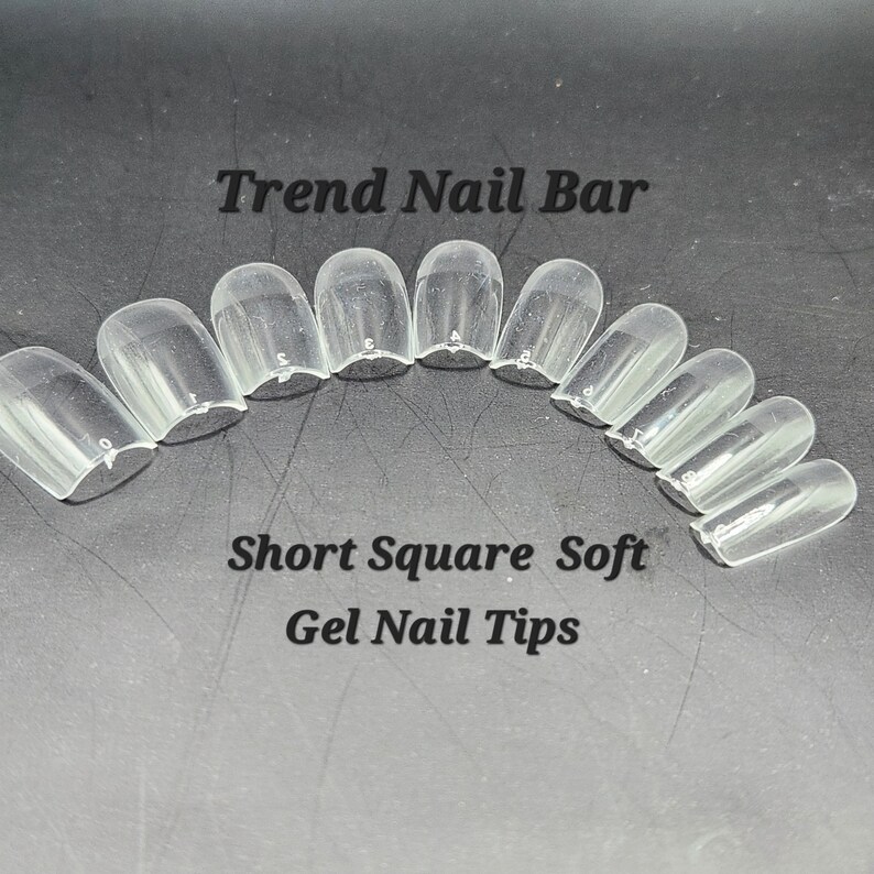 May include: Clear, short square soft gel nail tips arranged in an arc. The text "Trend Nail Bar" is at the top, and "Short Square Soft Gel Nail Tips" is at the bottom. Each tip is numbered.