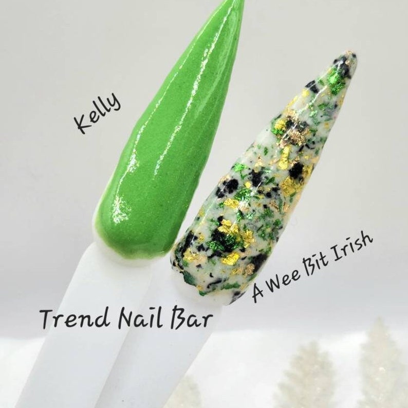 Pu&ograve; includere: Due colori di smalto per unghie, uno verde e uno bianco con glitter verde e oro. Lo smalto verde &egrave; etichettato "Kelly" e lo smalto glitterato &egrave; etichettato "A Wee Bit Irish". Lo smalto per unghie &egrave; mostrato su un bastoncino bianco con il testo "Trend Nail Bar" scritto su di esso.