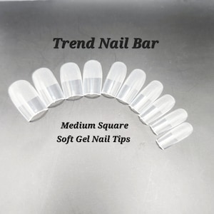 May include: A selection of clear, medium square soft gel nail tips. The tips are arranged in a semi-circle. The text "Trend Nail Bar" and "Medium Square Soft Gel Nail Tips" are displayed above and below the tips.