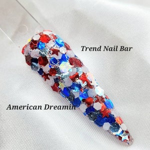 May include: Red, white, and blue glitter nail polish with a star-shaped design. The polish is called "American Dreamin'" and is from Trend Nail Bar.