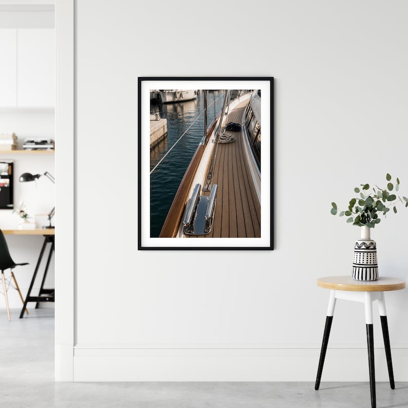 May include: A framed wall art print featuring a high-angle view of a yacht deck with teak wood planking, polished chrome hardware, and a stainless steel railing. The scene captures the side of the boat docked next to calm dark blue water.