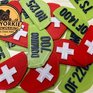 May include: A collection of green and red wooden dominoes with a Swiss cross design. The dominoes are numbered with black text, including "DOMINO 700", "OF 1400", "RO125", "OF 22", and "TS 55".