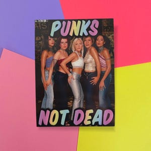 May include: A rectangular sticker with a group of women in various tops and jeans. The sticker has the words "PUNKS" and "NOT DEAD" in colourful bubble letters. The background is a mix of colours.
