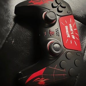 May include: Black PlayStation 5 controller with a red spider web design and the text "What's Up Danger" on the back.