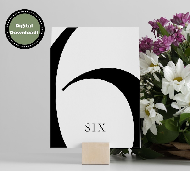 Puede incluir: Tarjeta de n&uacute;mero de mesa en blanco y negro con el n&uacute;mero seis y la palabra "SIX" impresa en negro. La tarjeta est&aacute; en un soporte de madera.