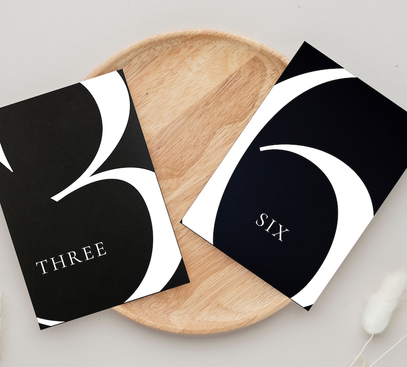 May include: Two black and white table number cards with a modern font. The card on the left says "THREE" and the card on the right says "SIX".