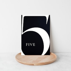 May include: Black and white table number card with the number "5" and the word "FIVE" in a modern font.