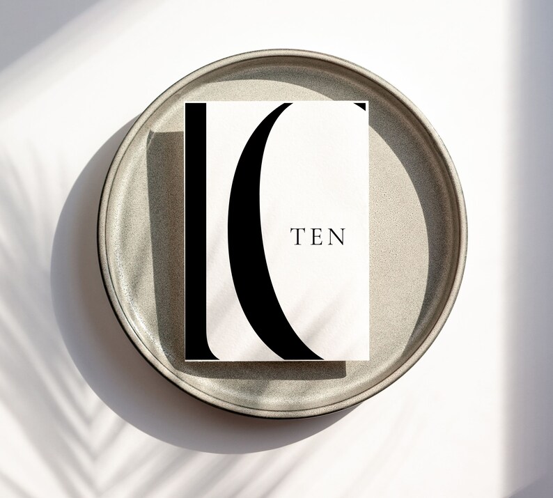 Puede incluir: Una tarjeta blanca con una letra C estilizada en negro y la palabra "TEN" impresa en negro. La tarjeta est&aacute; sobre un plato gris.
