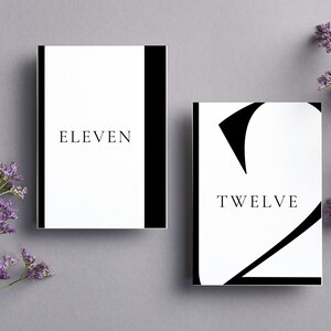 Puede incluir: Dos tarjetas de n&uacute;mero de mesa blancas con texto negro y bordes negros. La primera tarjeta dice "ELEVEN" y la segunda tarjeta dice "TWELVE" con un n&uacute;mero 2 negro estilizado.