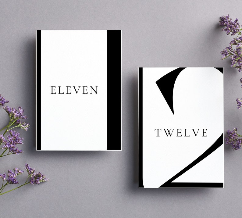 Puede incluir: Dos tarjetas de n&uacute;mero de mesa blancas con texto negro y bordes negros. La primera tarjeta dice "ELEVEN" y la segunda tarjeta dice "TWELVE" con un n&uacute;mero 2 negro estilizado.