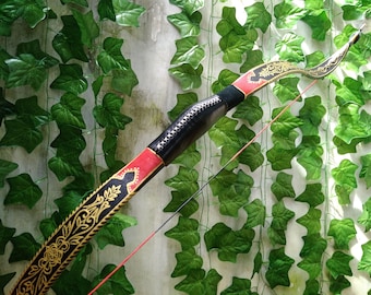 May include: A handcrafted recurve bow with a black, red, and gold design. The bow features intricate gold patterns and a black grip with white stitching. The bowstring is red and black, set against a backdrop of green ivy.
