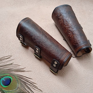 May include: A pair of brown leather arm guards with decorative embossed designs and silver buckles.
