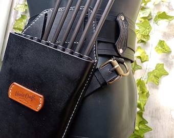 May include: A black leather quiver with a brown leather label that says "Hand-Craft" and a white stitch detail. The quiver is attached to a black leather belt with a metal buckle.
