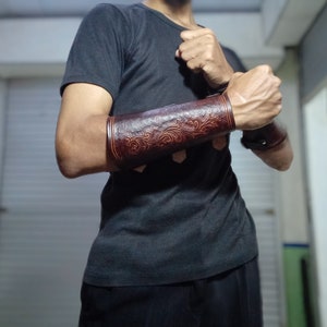 Könnte beinhalten: Ein braunes Lederarmband mit einem dekorativen floralen Design. Das Band wird am linken Arm einer Person getragen.