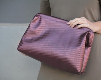 May include: A burgundy clutch bag with a textured, quilted design. The bag is made of a soft, supple material and has a simple, elegant style.