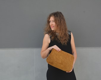 May include: A woman wearing a black sleeveless dress with a brown suede clutch.