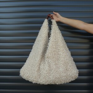 May include: A large, fluffy, off-white tote bag with brown leather handles. The bag is made of a soft, fuzzy material and has a relaxed, casual look.