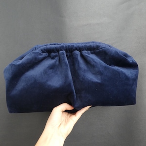 May include: A dark blue velvet clutch bag with a gathered top.