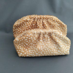 Może przedstawiać: Dwie miękkie torebki w kolorze opalenizny z białym nakrapianym wzorem. Każda torebka ma marszczone, zaokrąglone zamknięcie u góry i teksturowany wygląd przypominający tkaninę. Dwa przedmioty są umieszczone jeden za drugim.