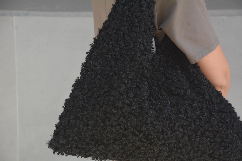 May include: A black fluffy tote bag made of faux fur. The bag is large and has a slouchy, unstructured shape.