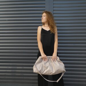 May include: A woman in a black dress holds a large, light beige, slouchy handbag with a long strap.