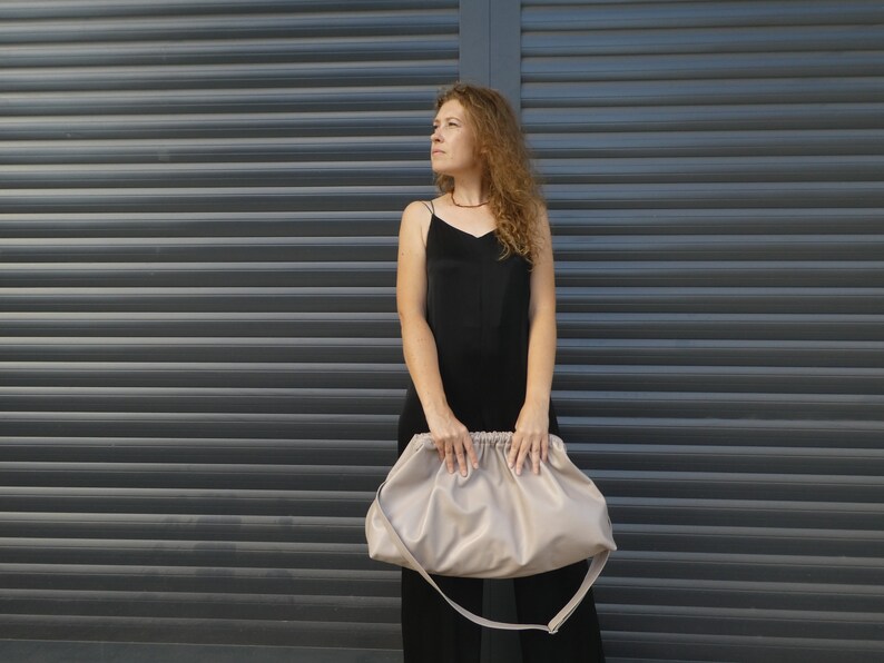 May include: A woman in a black dress holds a large, light beige, slouchy handbag with a long strap.