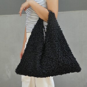 May include: A black fuzzy tote bag with a triangular shape. The bag is made of a soft, fluffy material.
