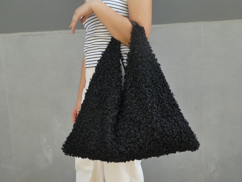May include: A black fuzzy tote bag with a triangular shape. The bag is made of a soft, fluffy material.