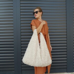 May include: A woman wearing a burnt orange dress and sunglasses holds a large, white, fluffy tote bag.