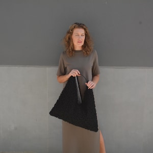 May include: A woman wearing a brown dress holds a black triangular-shaped handbag with a fuzzy texture.