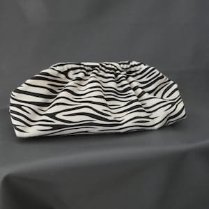 Peut inclure: Une pochette avec un motif à rayures zébrées noir et blanc. Le sac présente une ouverture supérieure souple, froncée et plissée, créant une silhouette arrondie en forme de bourse. Le tissu affiche un imprimé animal sur tout l'extérieur.