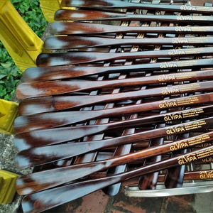 May include: A collection of dark brown wooden shoehorns arranged in a stack. Each shoehorn features a smooth, polished finish and is engraved with the text GLVIPA Greater Lehigh Valley Independent Practice Association, Inc. in gold lettering.