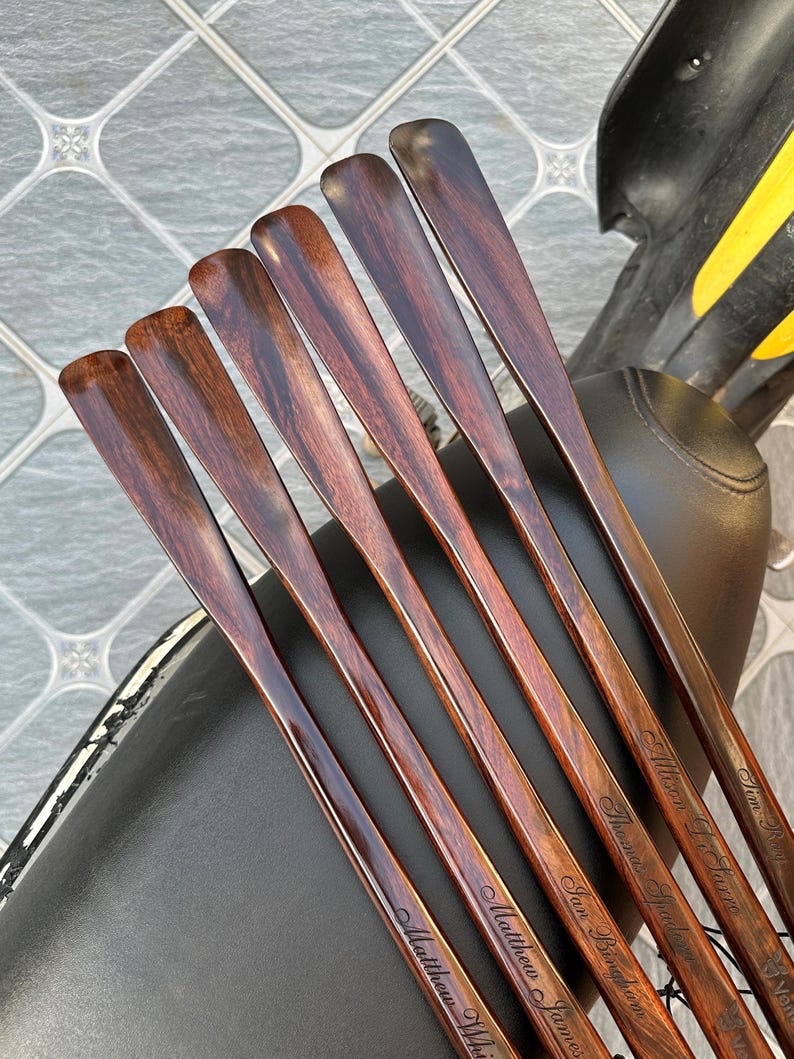 Pode incluir: Um conjunto de seis cal&ccedil;adeiras de madeira castanho-escura com acabamento polido e veios de madeira vis&iacute;veis. Cada cal&ccedil;adeira est&aacute; gravada com um nome &uacute;nico em letra cursiva, incluindo Matthew James, Ian Bingham, Thomas Spadaro e Allison L. Farre.