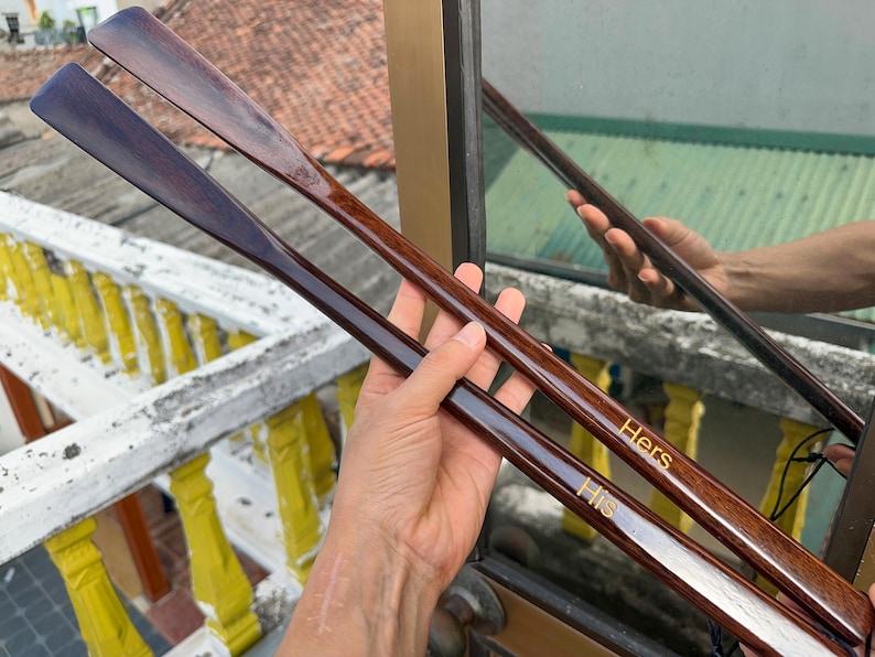 Pode incluir: Duas cal&ccedil;adeiras longas de madeira escura polida com um design liso e curvo. Uma cal&ccedil;adeira apresenta a palavra "His" gravada em letras douradas, enquanto a outra apresenta a palavra "Hers" gravada em letras douradas perto do cabo.