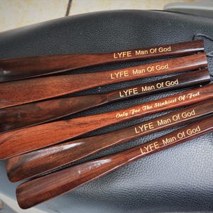 Pode incluir: Um conjunto de seis cal&ccedil;adeiras de madeira castanho-escura com acabamento liso. Cinco cal&ccedil;adeiras est&atilde;o gravadas com o texto LYFE Man Of God, e uma com o texto Only For The Stinkiest Of Feet. Cada uma tem um cord&atilde;o preto preso.