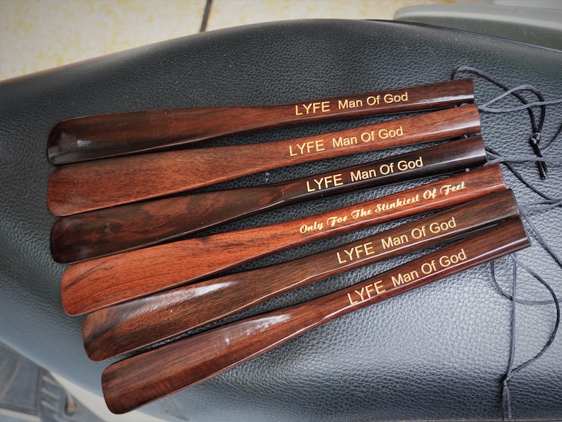 Pode incluir: Um conjunto de seis cal&ccedil;adeiras de madeira castanho-escura com acabamento liso. Cinco cal&ccedil;adeiras est&atilde;o gravadas com o texto LYFE Man Of God, e uma com o texto Only For The Stinkiest Of Feet. Cada uma tem um cord&atilde;o preto preso.