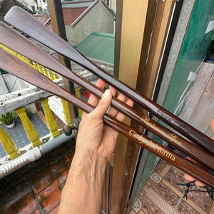 Pode incluir: Tr&ecirc;s cal&ccedil;adeiras longas de madeira castanho-escura com superf&iacute;cies lisas e polidas. Cada cal&ccedil;adeira apresenta um nome ou frase gravada numa fonte cursiva de cor dourada no cabo, incluindo Cody & Norma, Batman Shen e Owen Chen.
