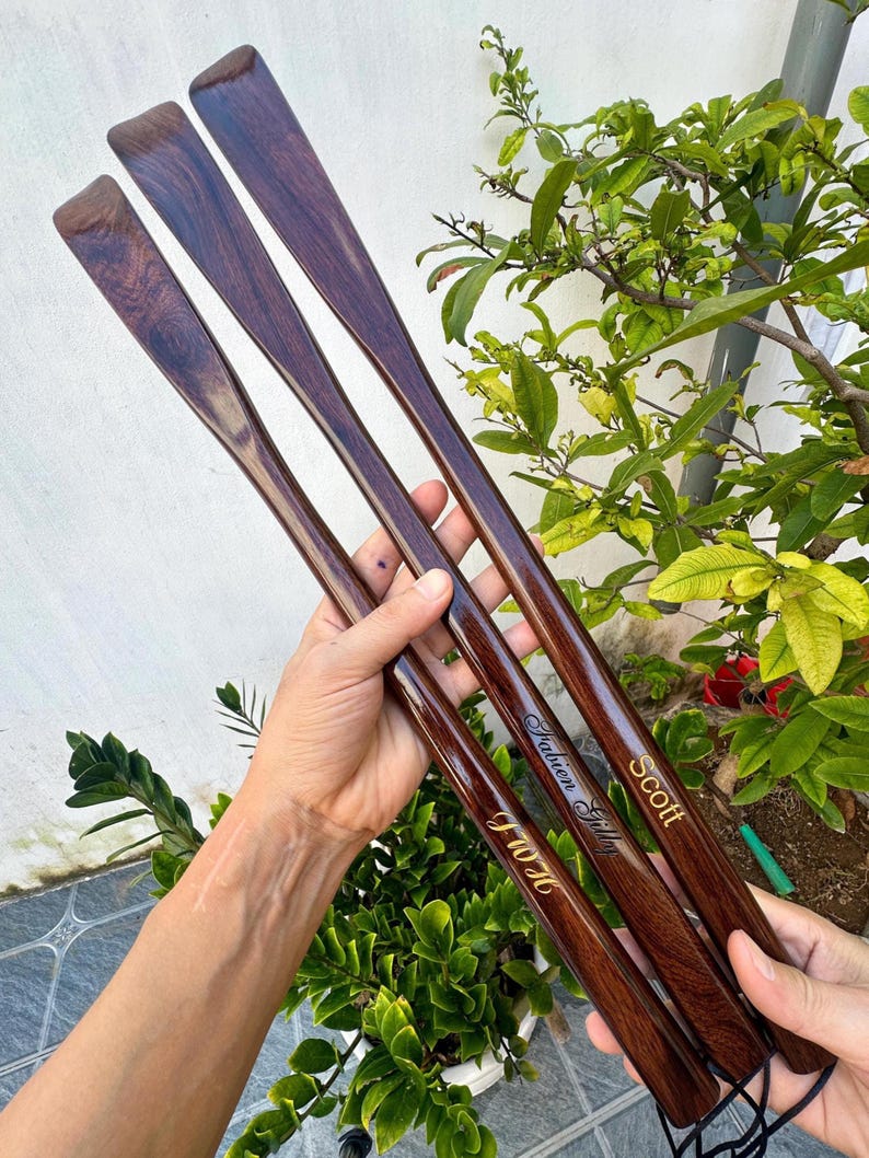 Pode incluir: Tr&ecirc;s cal&ccedil;adeiras longas de madeira castanho-escura com acabamento polido. Cada cal&ccedil;adeira apresenta um nome gravado em letras douradas: Scott, Fabien Gilly e J W H. As cal&ccedil;adeiras est&atilde;o unidas na base por um cord&atilde;o preto fino.